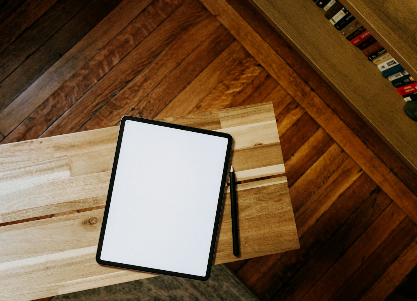 A tablet and stylus rest on a light wooden table.